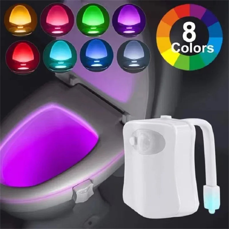 LED toilet night light glowing in soft colors attached to toilet bowl in a dark bathroom
